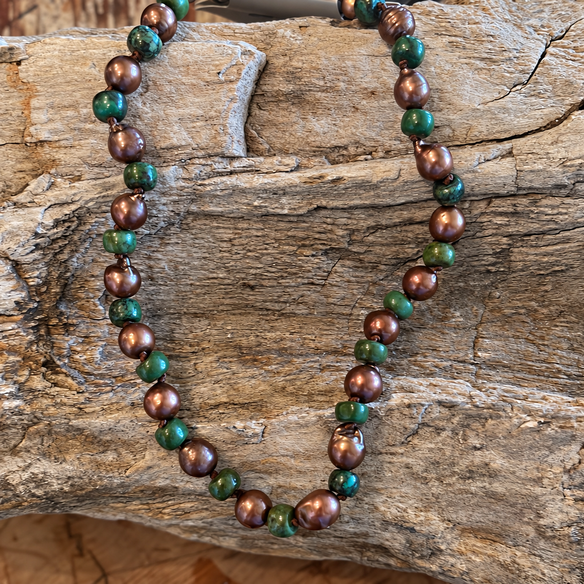 African turquoise necklace with green stone beads and bronze-colored accent beads on rustic wood
