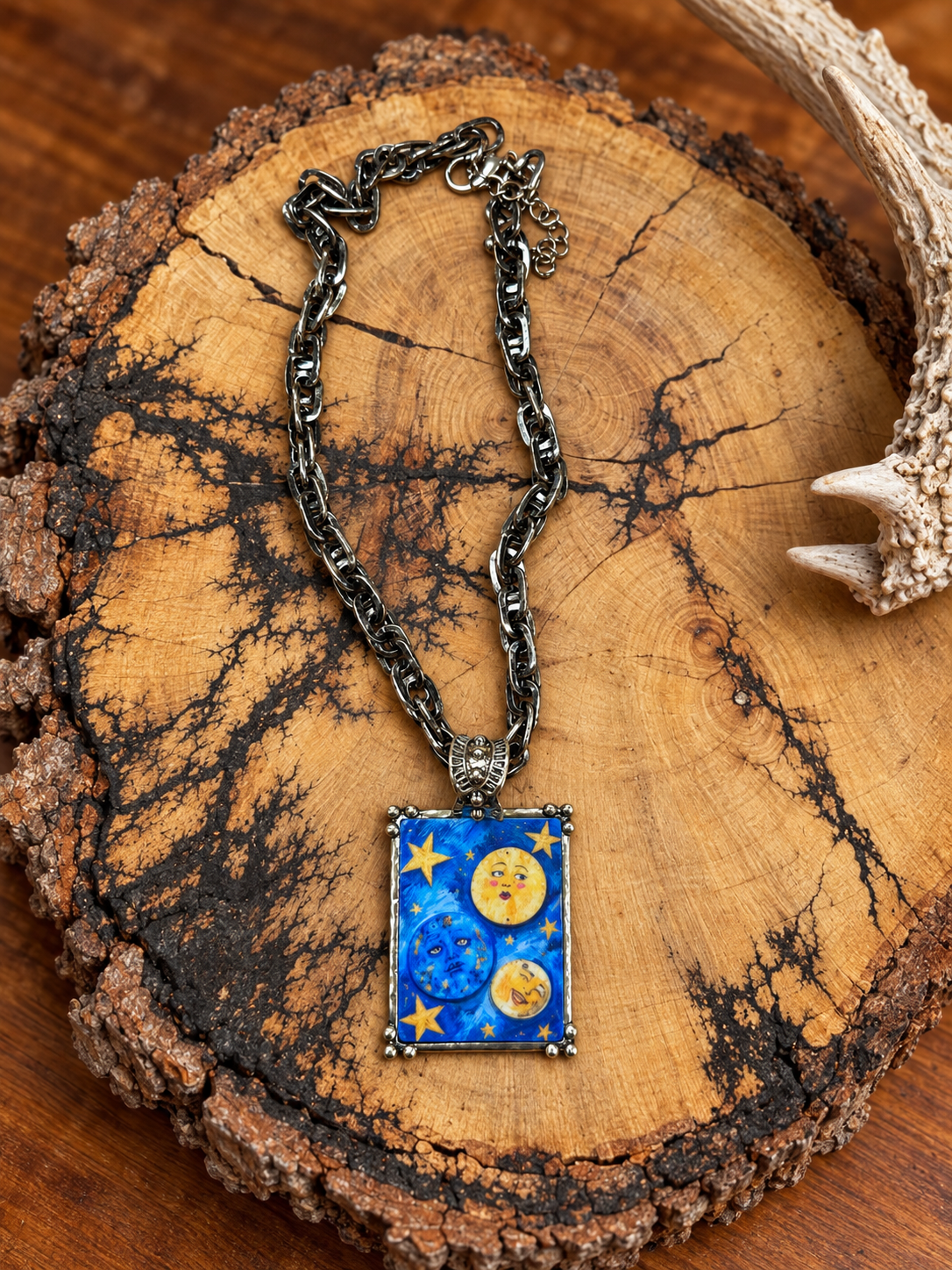 Blue celestial pendant necklace with yellow stars and antiqued silver-tone chain on rustic wood