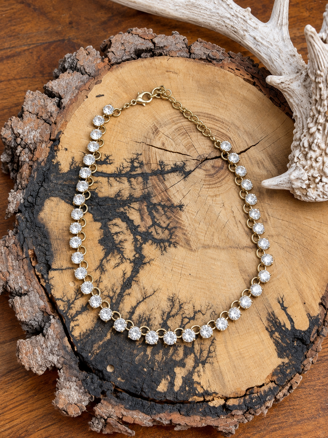 Clear round crystal link necklace with gold-tone links and extender on a rustic wood slice