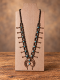 Copper-Tone & Turquoise Concho Statement Necklace displayed on a jewelry stand against a warm wood tabletop and softly blurred brown background