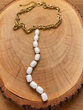Gold-tone chain necklace with long white pearl-look drop on natural wood