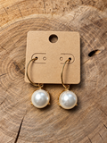 Gold-tone pearl-look drop hoop earrings on a plain kraft card