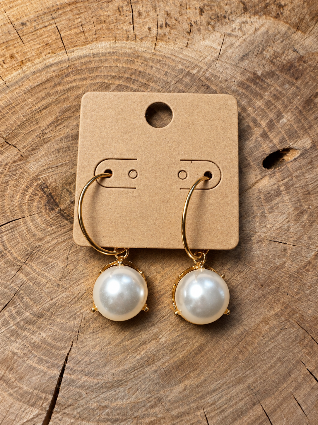Gold-tone pearl-look drop hoop earrings on a plain kraft card