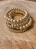 Five-piece gold-tone bracelet set with two rhinestone bracelets and three beaded bracelets on wood