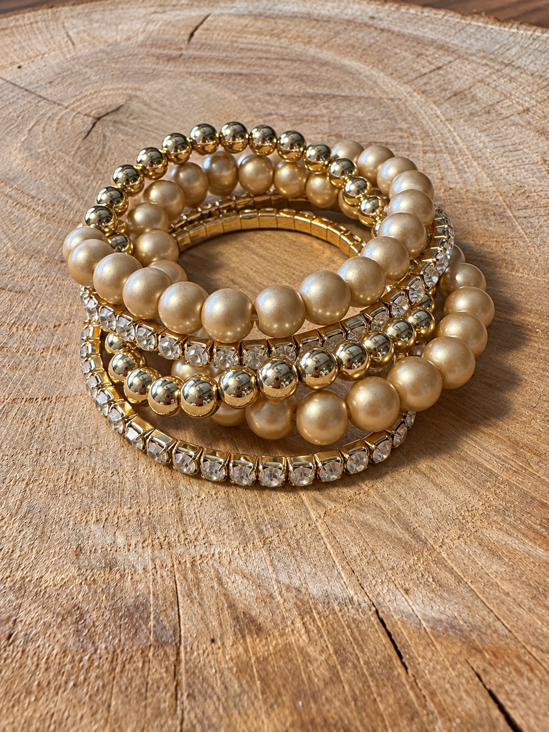 Five-piece gold-tone bracelet set with two rhinestone bracelets and three beaded bracelets on wood