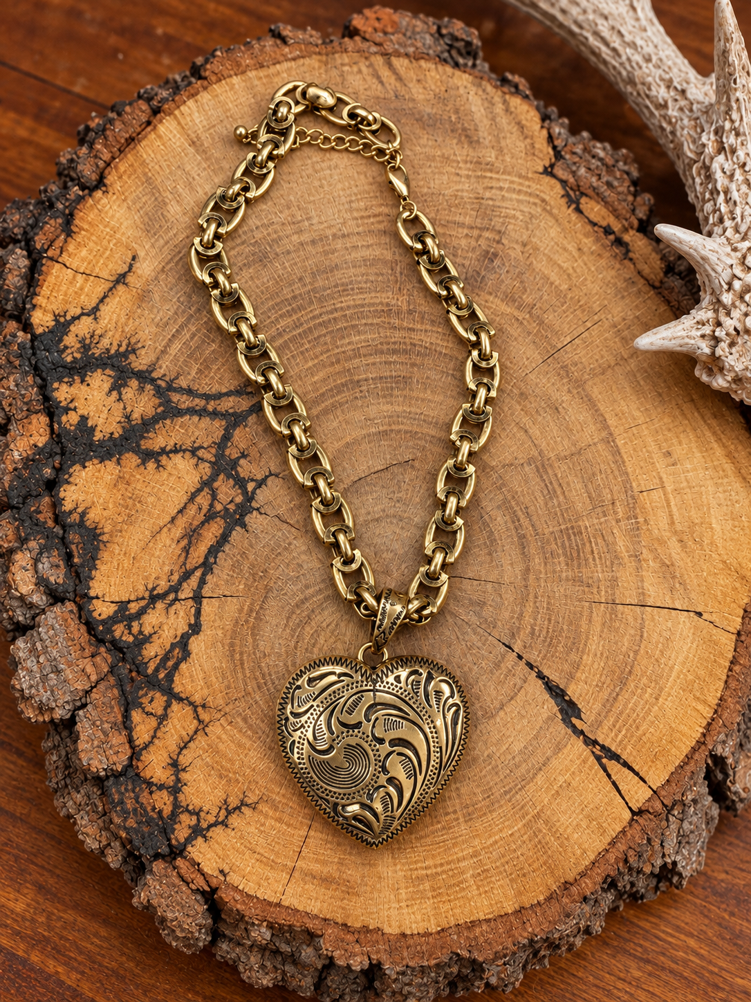 Antiqued gold-tone western scroll heart pendant necklace on a rustic bark-edged wood slice