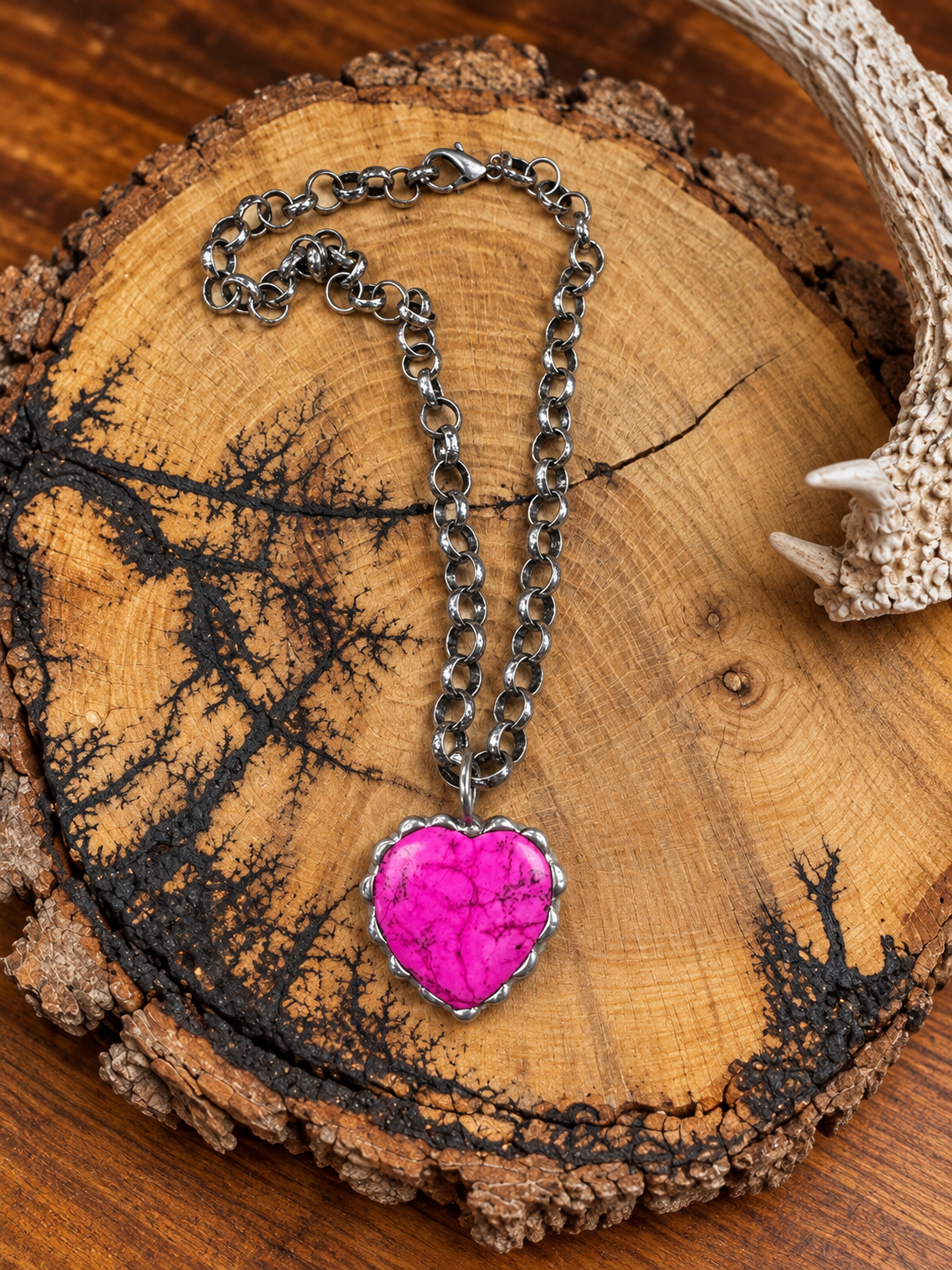 Hot pink marbled heart pendant on a silver-tone chain displayed on a rustic wood slice