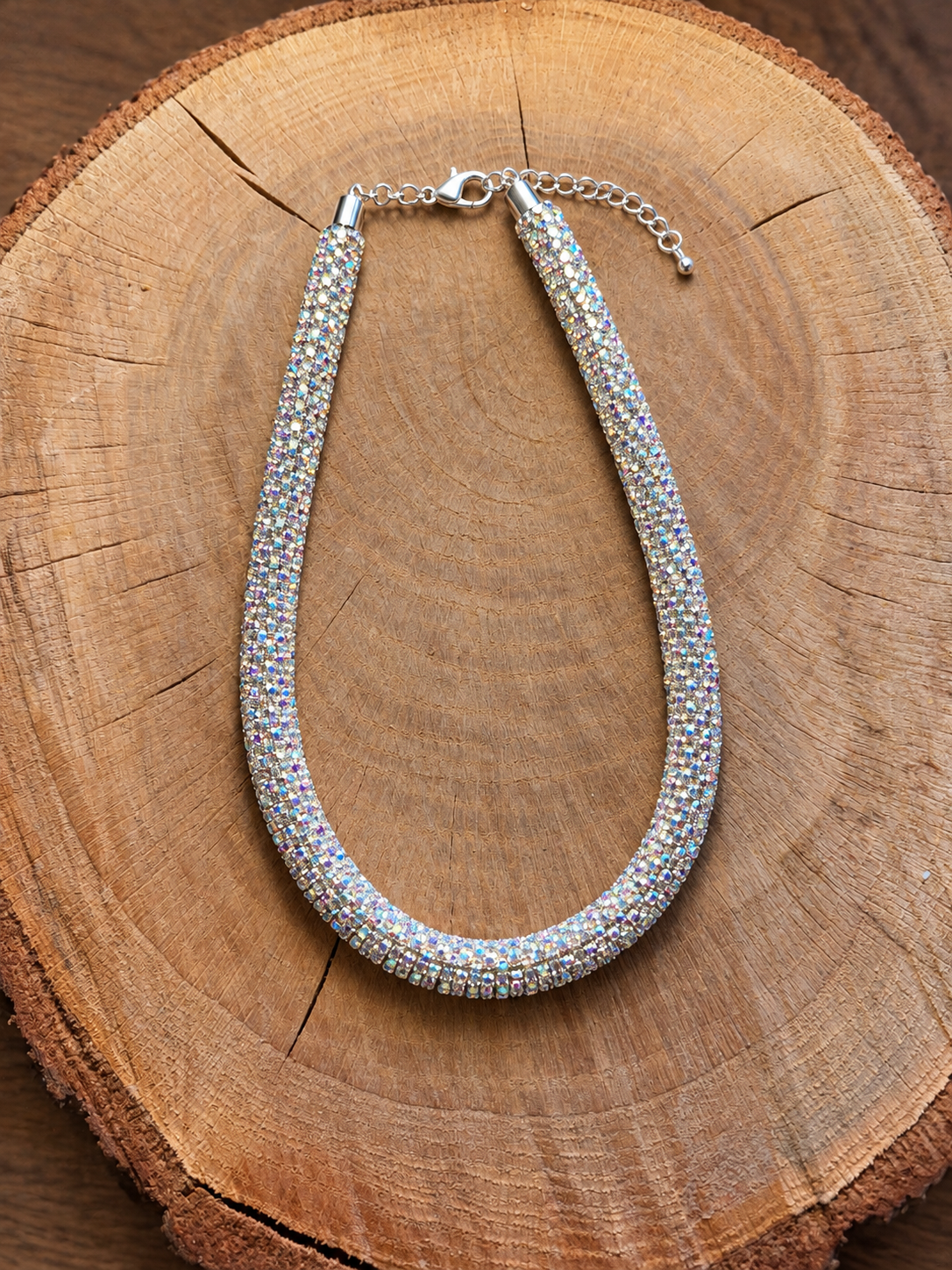 Iridescent rhinestone rope necklace with silver-tone clasp on natural wood