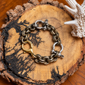 Gold-tone textured chain bracelet with silver-tone snaffle hardware on rustic wood