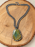 Olive green faceted hand-soldered pendant necklace on a rustic wood display