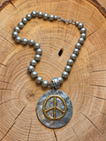 Gold-tone peace sign silver medallion beaded necklace on wood