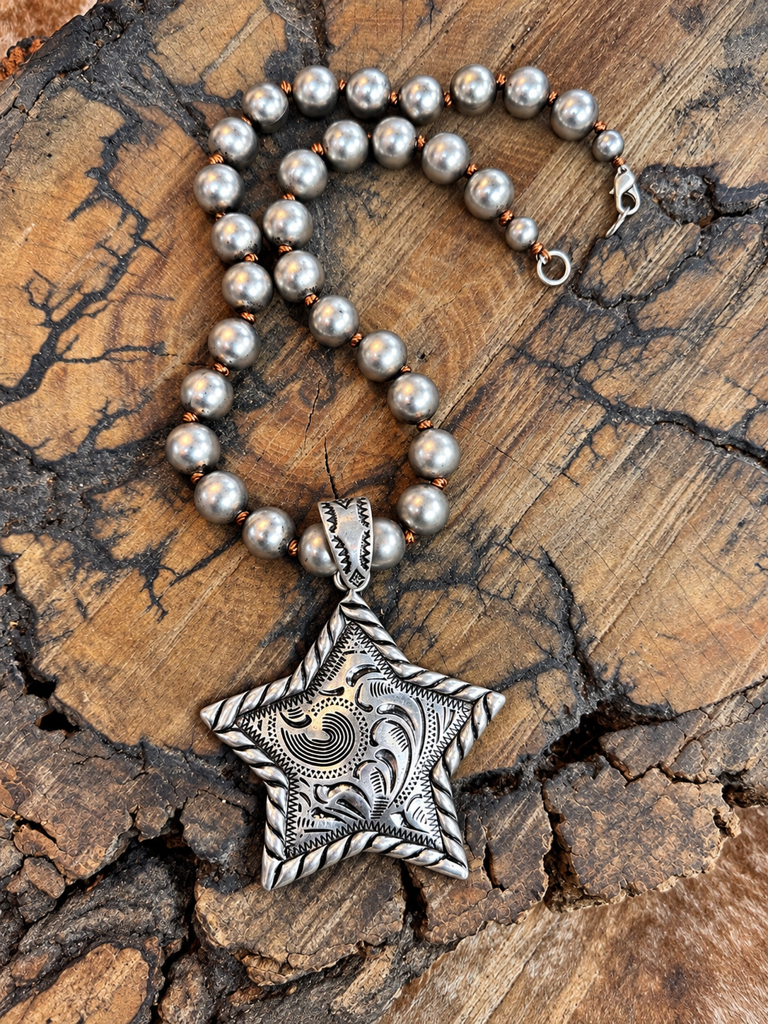 Engraved silver-tone star pendant on a hand-knotted faux Navajo pearl necklace on rustic wood