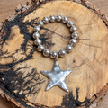 Silver-tone beaded bracelet with a large silver star charm on a rustic wood slice