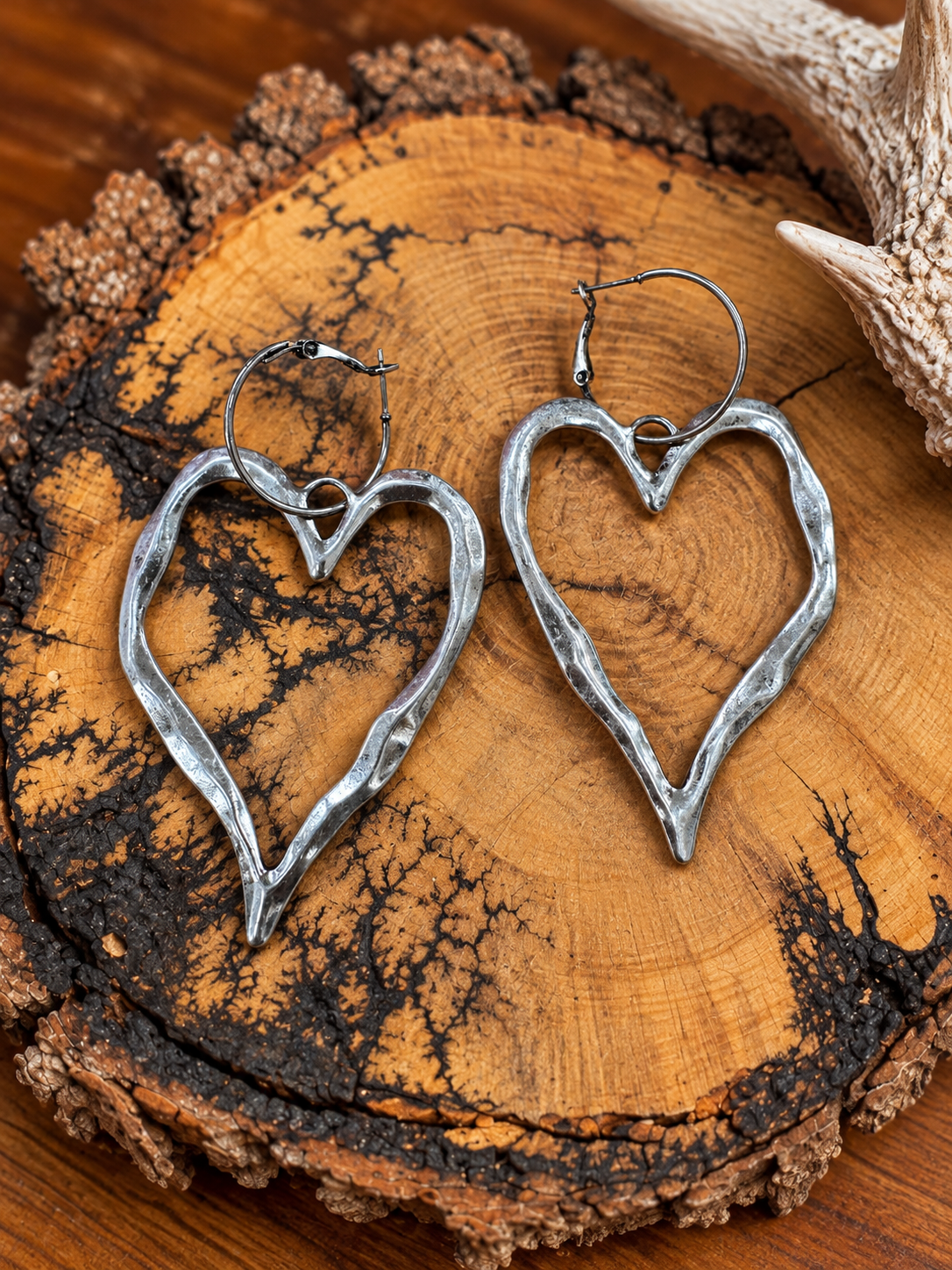 Silver-tone open heart hoop earrings on a rustic wood slice with an antler accent