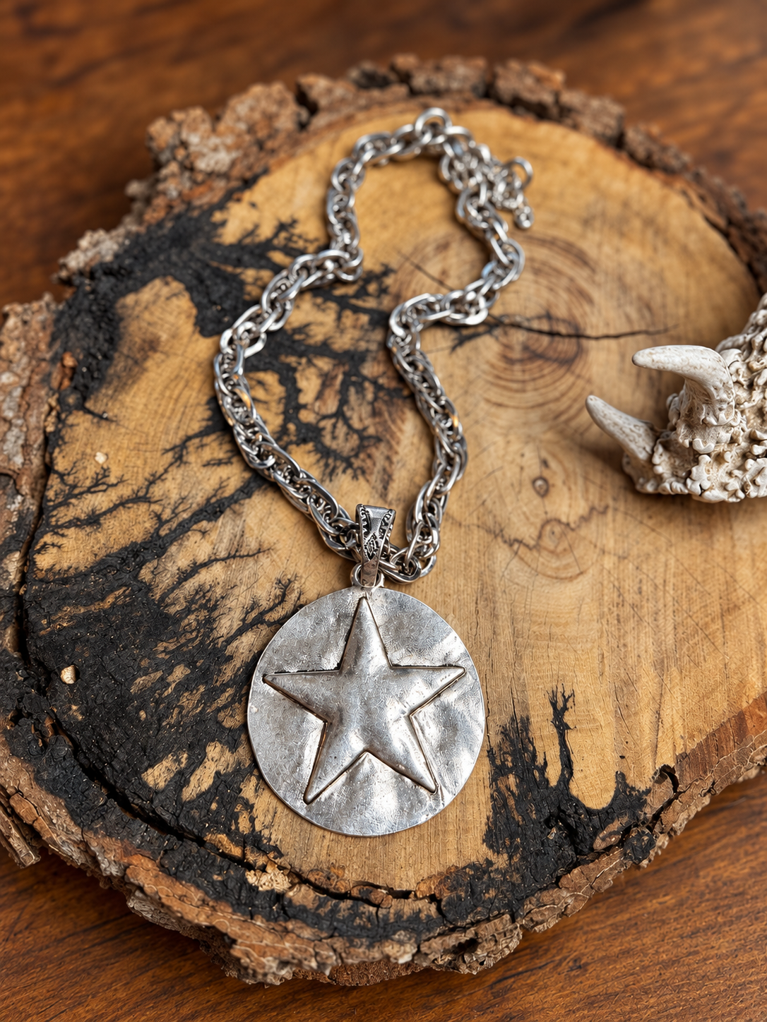 Silver-tone star medallion necklace with an engraved bail and layered link chain on rustic wood