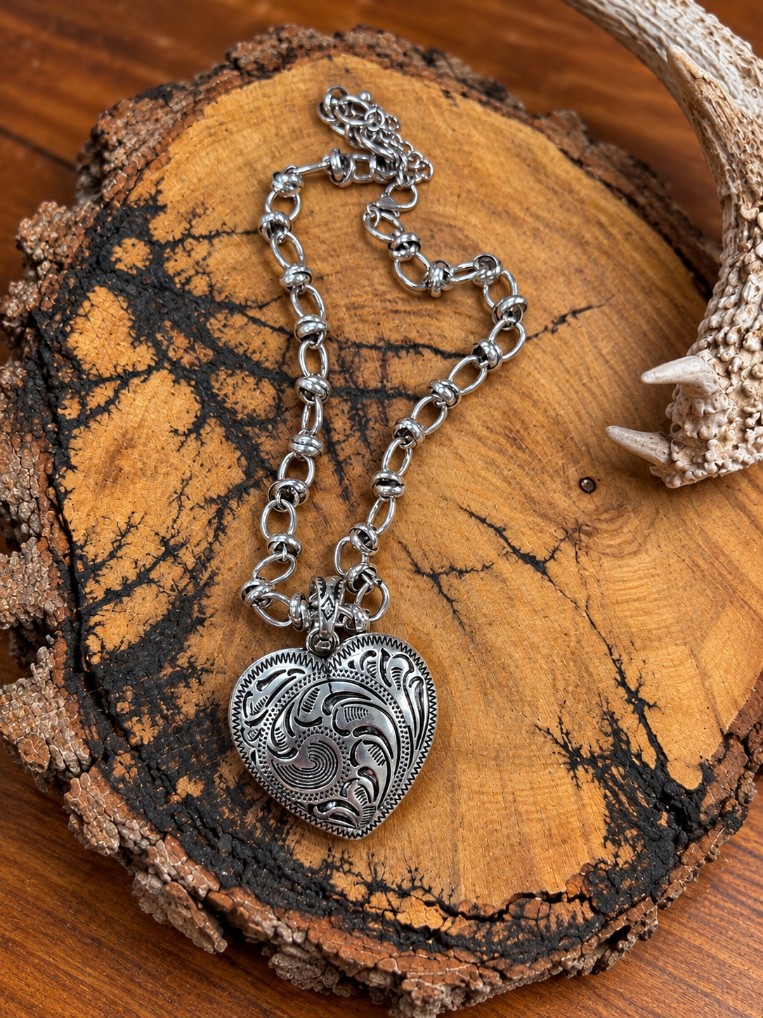 Silver-tone western scroll heart necklace displayed on a bark-edged wood slice with an antler accent
