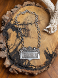Ornate silver-tone TEQUILA pendant necklace with textured oval links on rustic wood