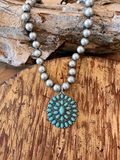 Chunky silver-tone beaded necklace with an oval turquoise-colored cluster pendant on rustic wood