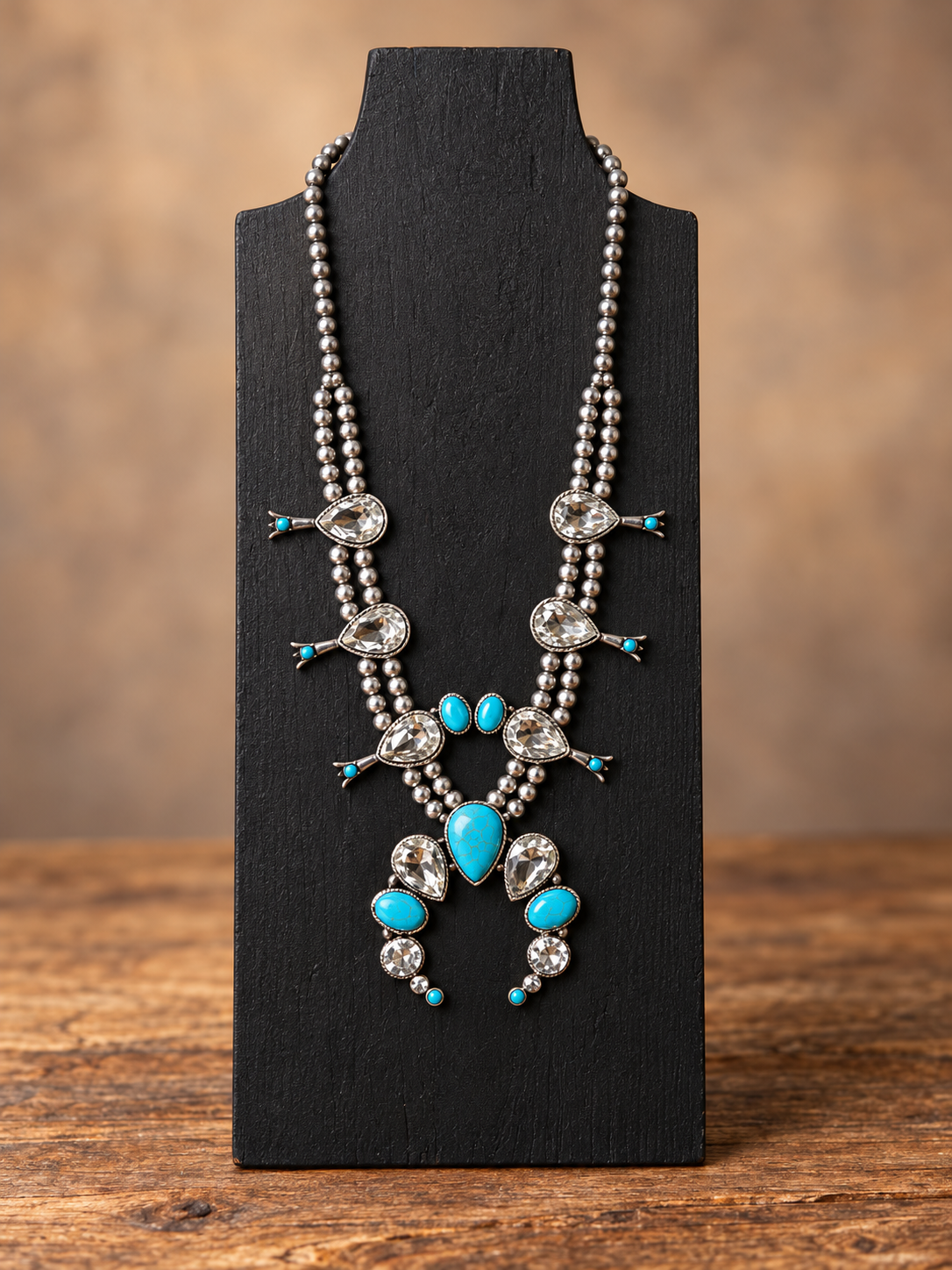 Silver-tone beaded necklace with turquoise-colored accents and clear teardrop crystals on a black jewelry stand