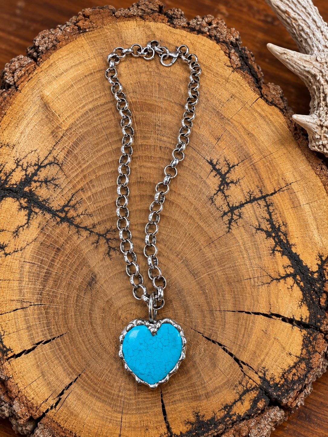 Turquoise-color heart pendant on a silver-tone link chain displayed on a rustic wood slice