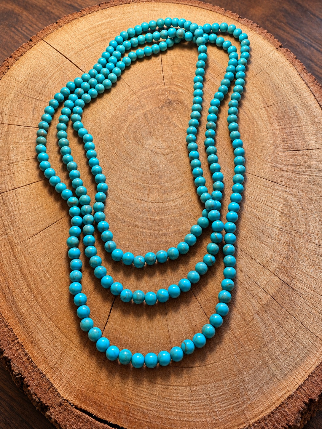 Turquoise-color round bead necklace arranged in layered loops on natural wood