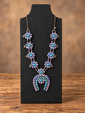 Turquoise & Iridescent Floral Statement Necklace displayed on a jewelry stand against a warm wood tabletop and softly blurred brown background