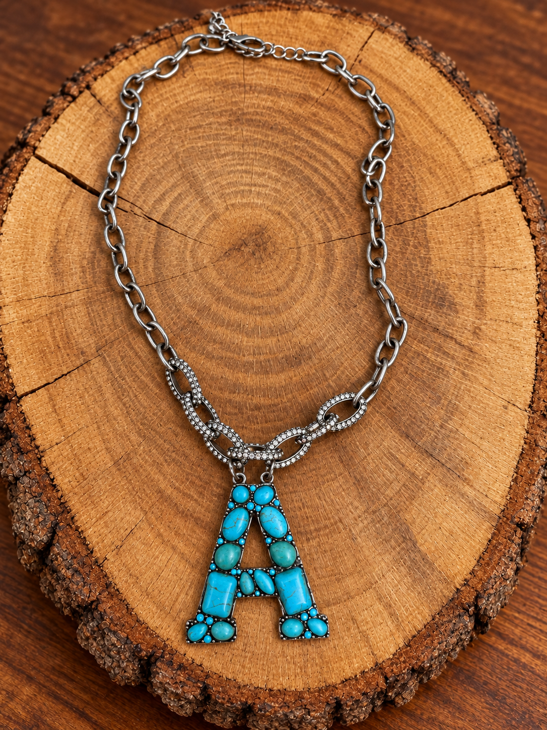 Turquoise letter A pendant with rhinestone accents on a silver-tone chain, displayed on warm rustic wood