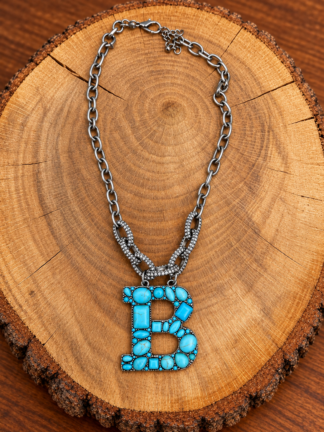 Turquoise letter B pendant with rhinestone accents on a silver-tone chain, displayed on warm rustic wood