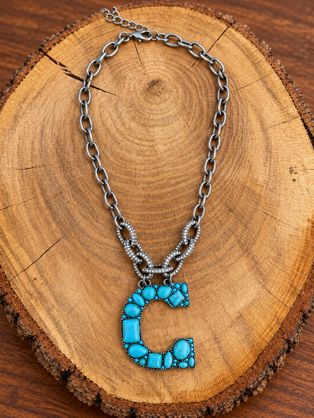 Turquoise letter C pendant with rhinestone accents on a silver-tone chain, displayed on warm rustic wood