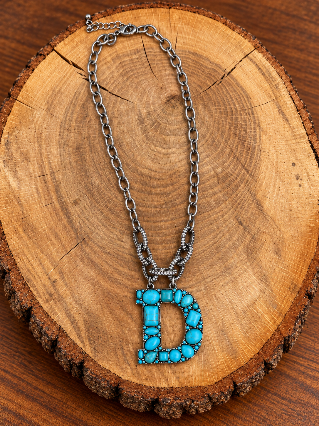 Turquoise letter D pendant with rhinestone accents on a silver-tone chain, displayed on warm rustic wood