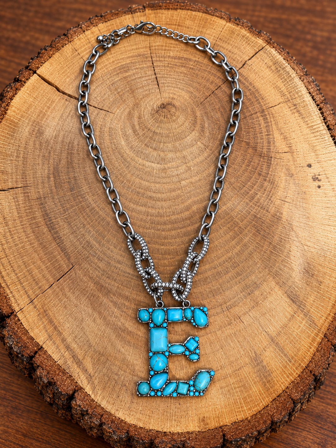 Turquoise letter E pendant with rhinestone accents on a silver-tone chain, displayed on warm rustic wood