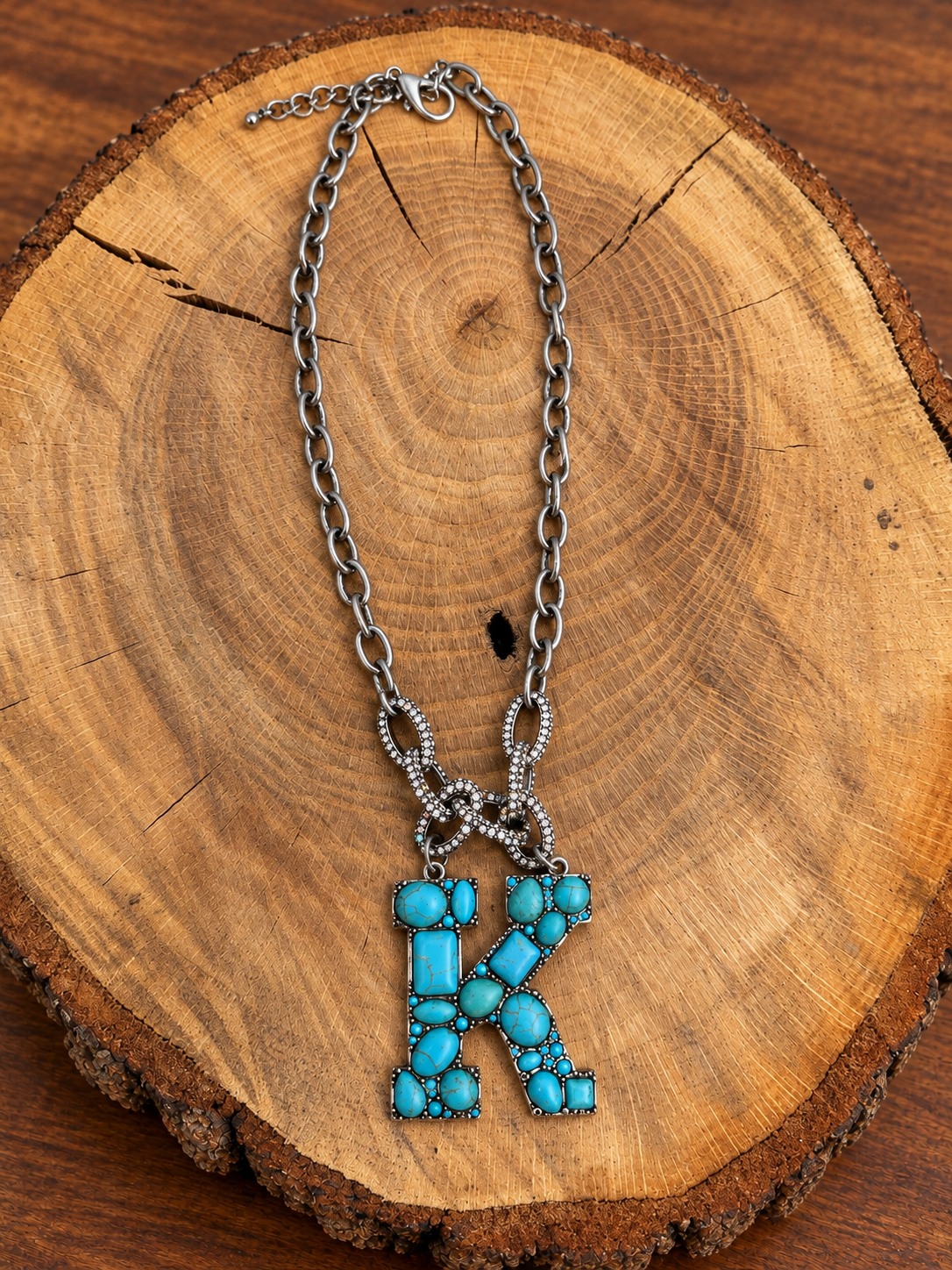 Turquoise letter K pendant with rhinestone accents on a silver-tone chain, displayed on warm rustic wood
