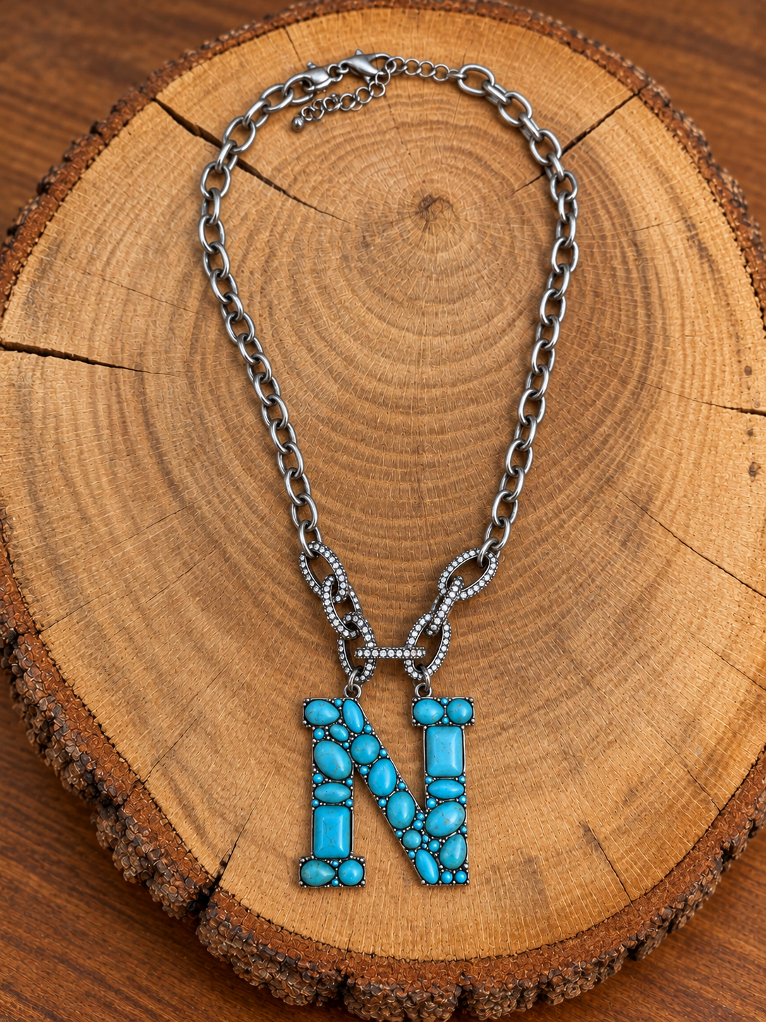 Turquoise letter N pendant with rhinestone accents on a silver-tone chain, displayed on warm rustic wood