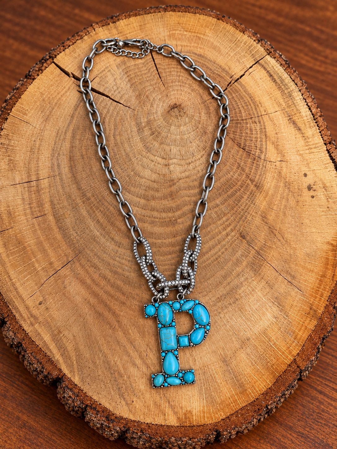 Turquoise letter P pendant with rhinestone accents on a silver-tone chain, displayed on warm rustic wood