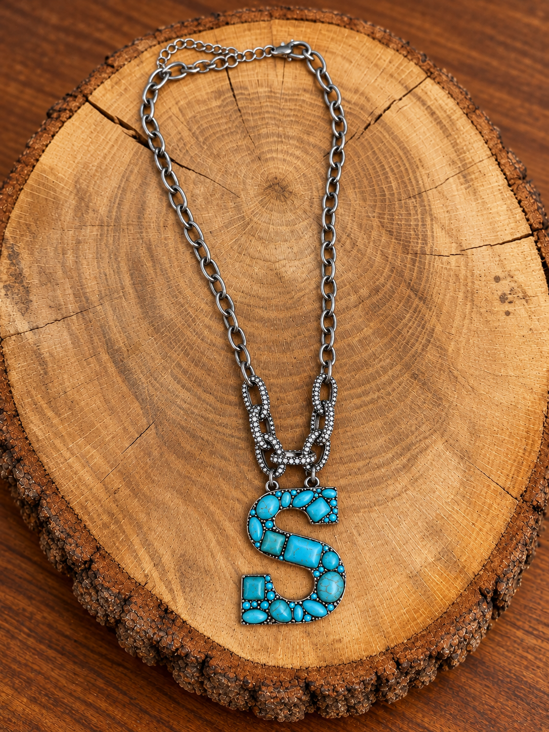 Turquoise letter S pendant with rhinestone accents on a silver-tone chain, displayed on warm rustic wood