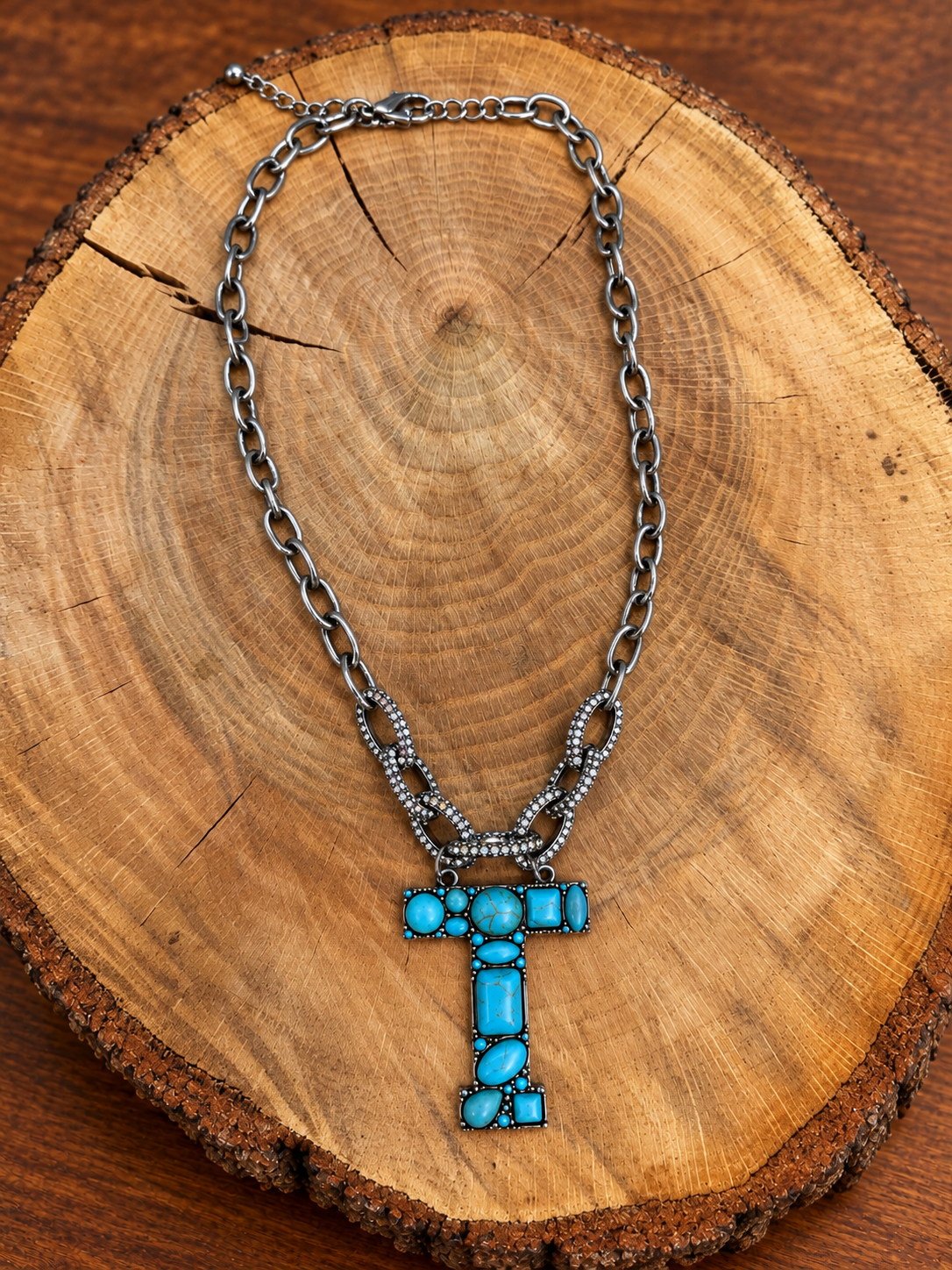 Turquoise letter T pendant with rhinestone accents on a silver-tone chain, displayed on warm rustic wood