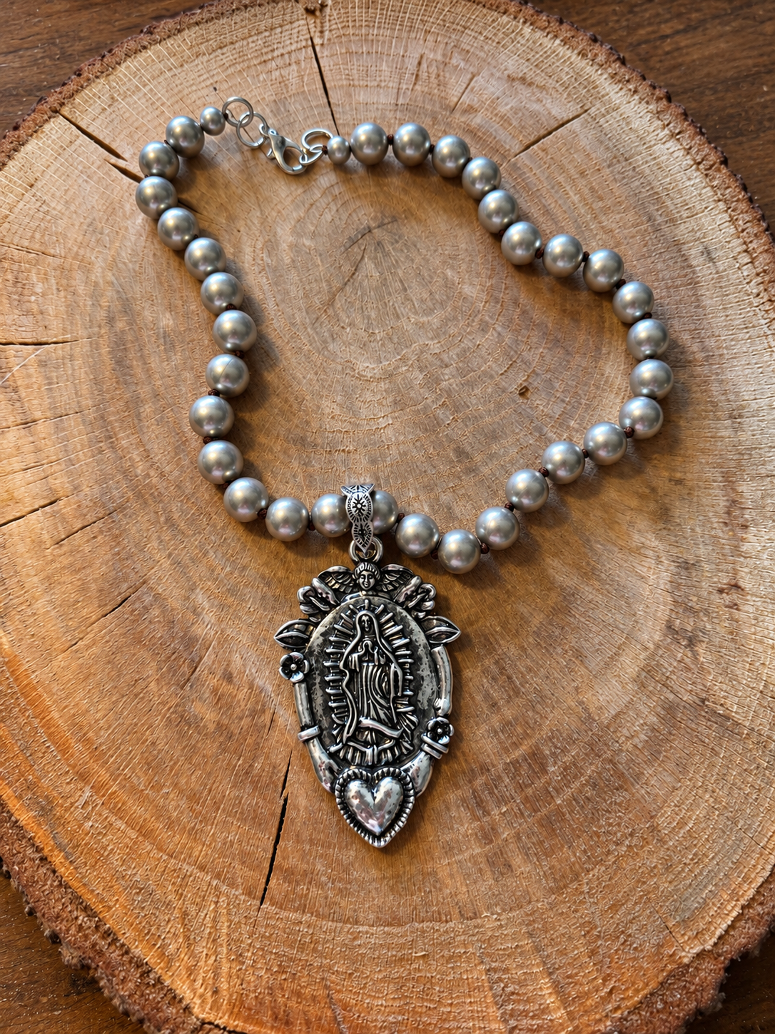 Virgin Mary and Heart silver-tone beaded necklace on natural wood